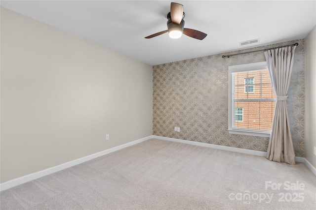 empty room featuring visible vents, a ceiling fan, carpet floors, wallpapered walls, and baseboards