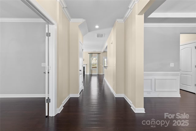 hallway with crown molding, a decorative wall, visible vents, and dark wood-style flooring