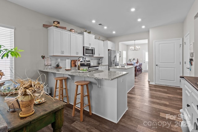 kitchen with a healthy amount of sunlight, dark wood-style floors, a peninsula, stainless steel appliances, and a center island