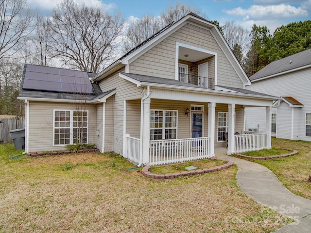 view of front facade with a porch, a front lawn, a balcony, and roof mounted solar panels