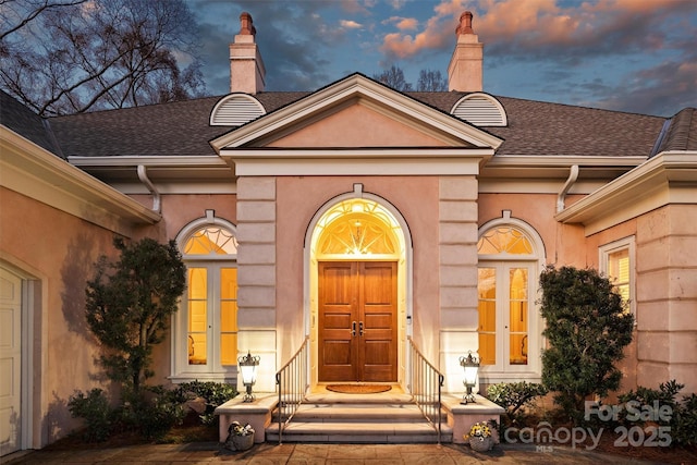 view of exterior entry with french doors, a chimney, and a shingled roof