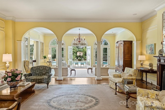 living area with decorative columns, wood finished floors, a chandelier, and ornamental molding