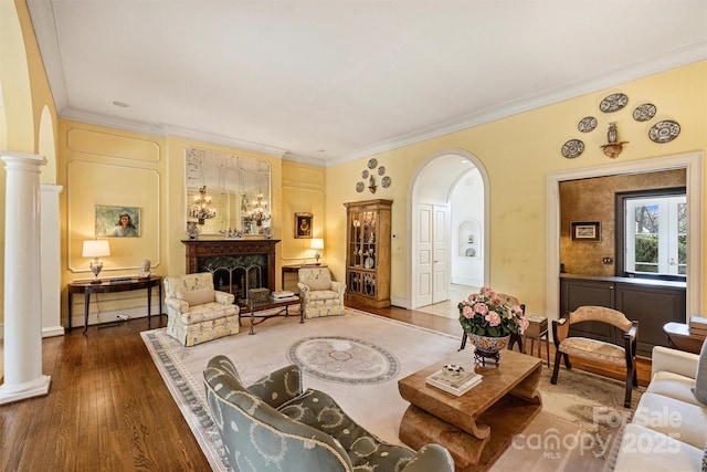 living room with ornamental molding, decorative columns, a fireplace, wood finished floors, and arched walkways