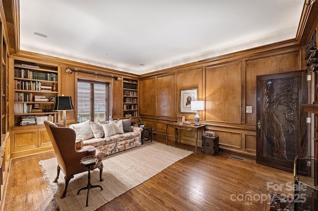 sitting room with a decorative wall, built in shelves, visible vents, and wood finished floors