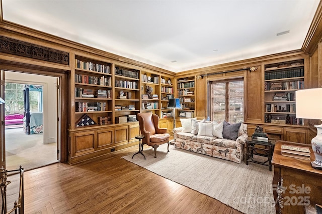 sitting room with built in shelves, crown molding, and wood finished floors