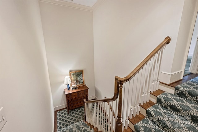 staircase with wood finished floors, baseboards, and ornamental molding