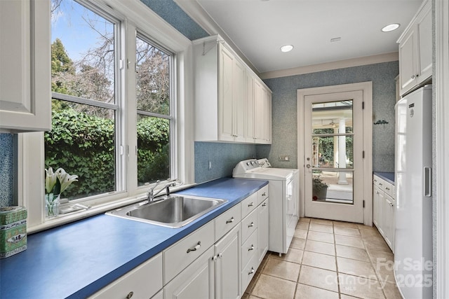 clothes washing area with a wealth of natural light, a sink, cabinet space, wallpapered walls, and washing machine and clothes dryer