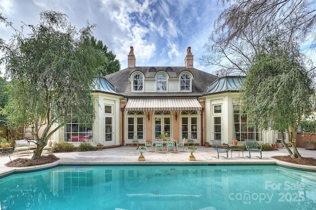 back of house with stucco siding, a standing seam roof, a patio, an outdoor pool, and a chimney