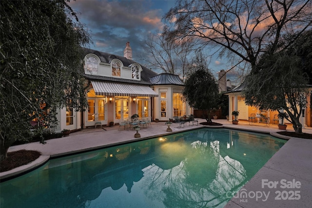 pool at dusk with a patio, french doors, and an outdoor pool