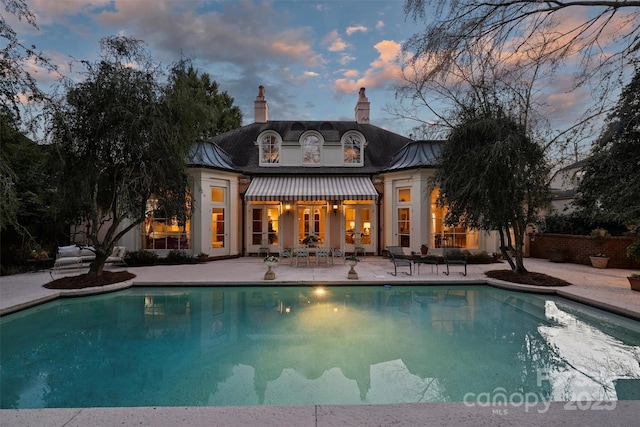 pool at dusk featuring an outdoor pool, french doors, and a patio