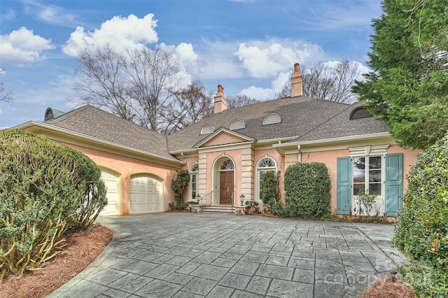 view of front of house with stucco siding, an attached garage, a chimney, and driveway