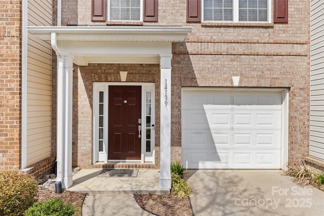 doorway to property featuring concrete driveway, an attached garage, and brick siding