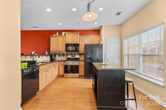 kitchen featuring visible vents, black appliances, a sink, tasteful backsplash, and a center island