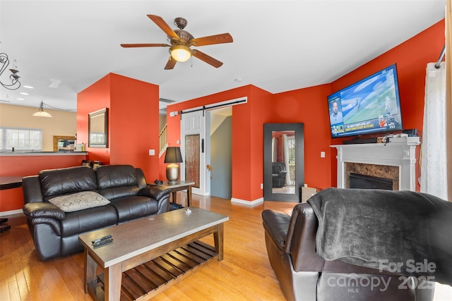 living area featuring baseboards, light wood-style flooring, a fireplace, ceiling fan, and a barn door