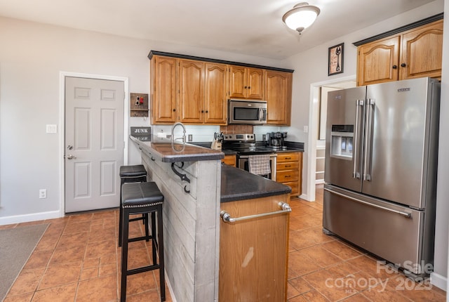 kitchen with dark countertops, light tile patterned floors, a kitchen breakfast bar, appliances with stainless steel finishes, and a peninsula