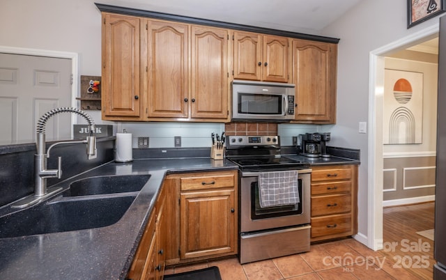 kitchen with light tile patterned floors, brown cabinets, appliances with stainless steel finishes, and a sink