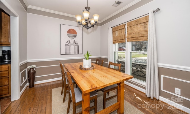 dining room featuring wood finished floors, baseboards, visible vents, crown molding, and a chandelier