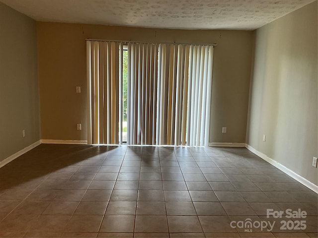 tiled empty room featuring baseboards and a textured ceiling