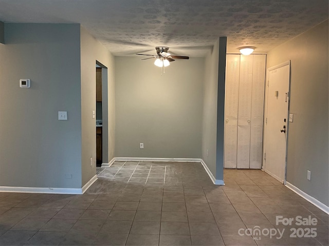 spare room with dark tile patterned floors, ceiling fan, baseboards, and a textured ceiling