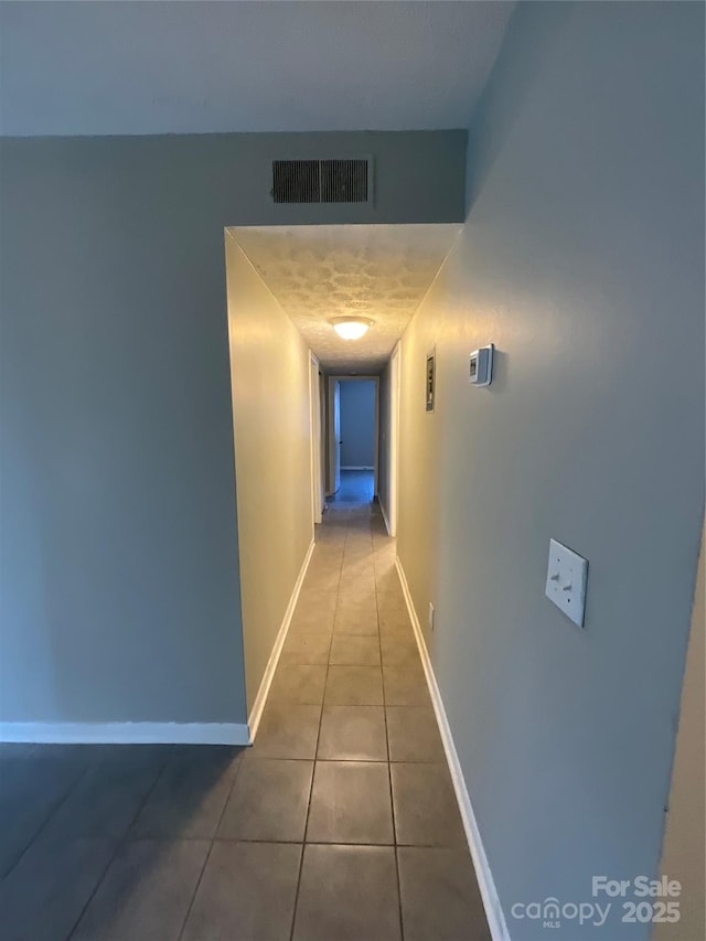 hallway with baseboards, visible vents, a textured ceiling, and tile patterned floors