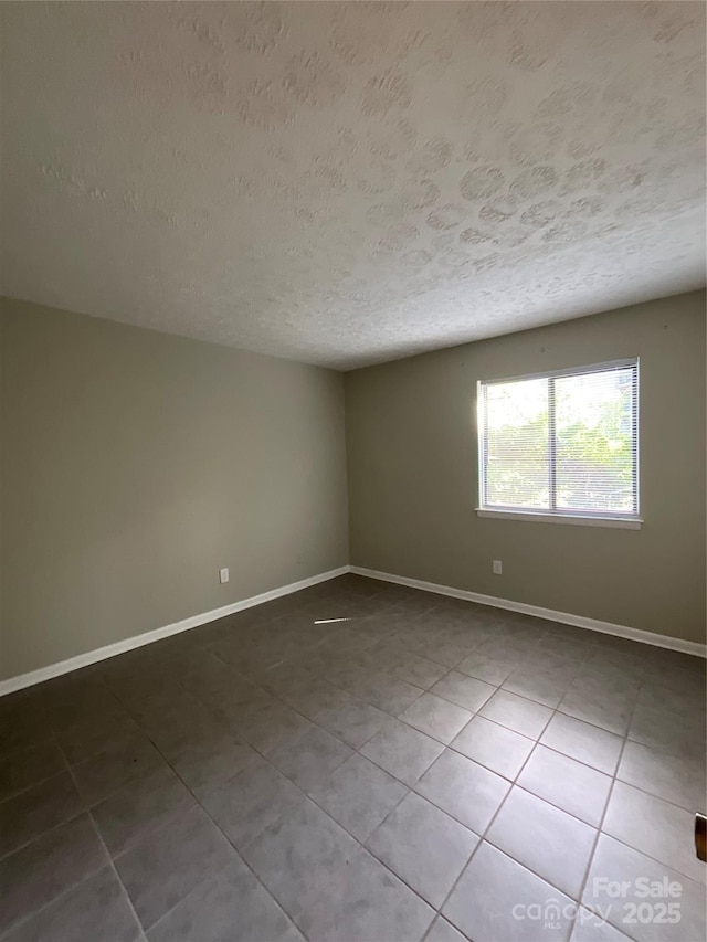 empty room with a textured ceiling, tile patterned flooring, and baseboards