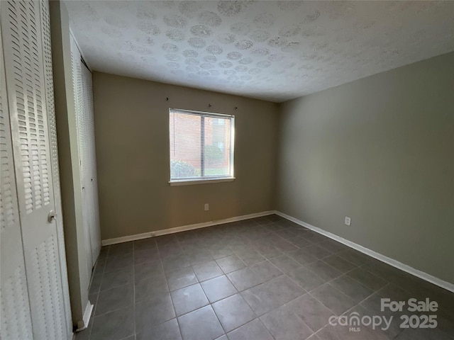 unfurnished bedroom with tile patterned flooring, baseboards, and a textured ceiling