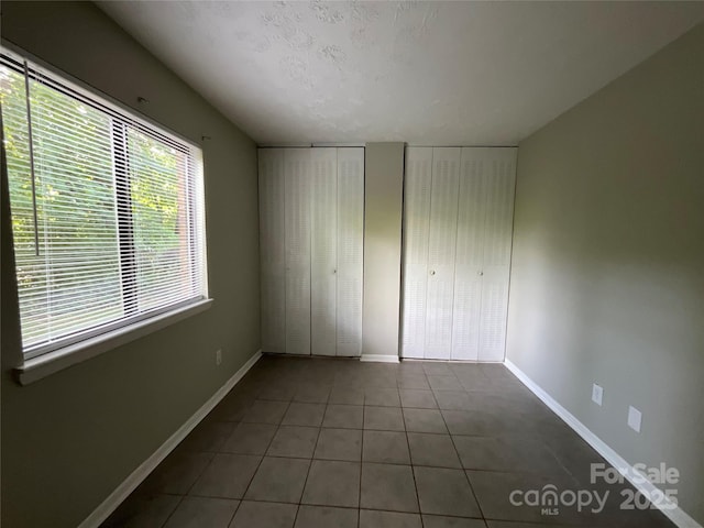 unfurnished bedroom with multiple closets, tile patterned flooring, and baseboards