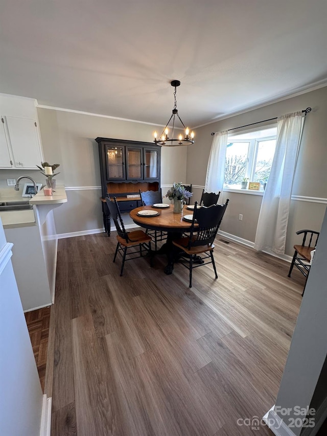 dining space with baseboards, a notable chandelier, wood finished floors, and ornamental molding