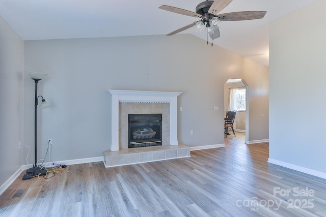 unfurnished living room with wood finished floors, baseboards, a fireplace, arched walkways, and vaulted ceiling