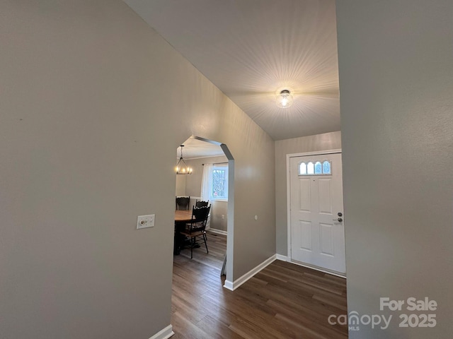 foyer entrance featuring baseboards, arched walkways, and dark wood finished floors