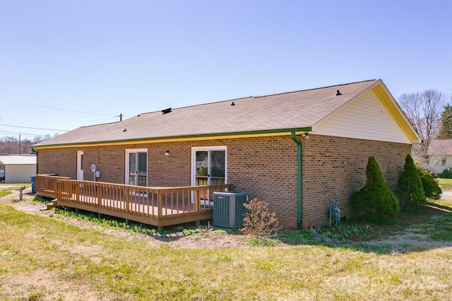 rear view of house with cooling unit, brick siding, a deck, and a yard