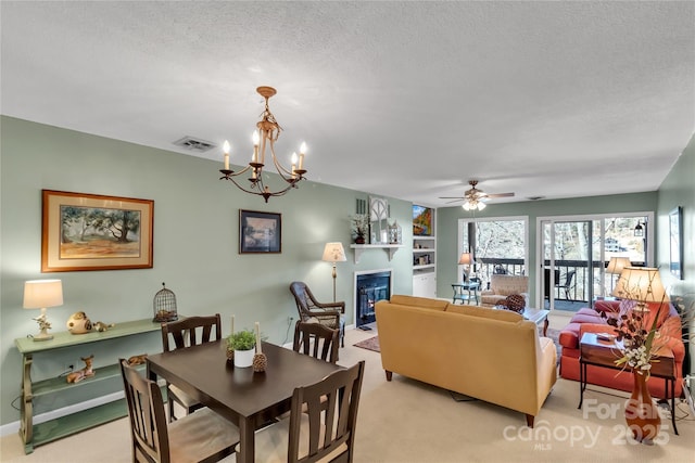 dining area featuring visible vents, light colored carpet, ceiling fan with notable chandelier, a glass covered fireplace, and a textured ceiling