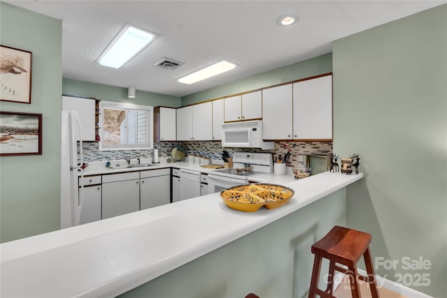 kitchen with tasteful backsplash, visible vents, a breakfast bar area, white appliances, and a sink