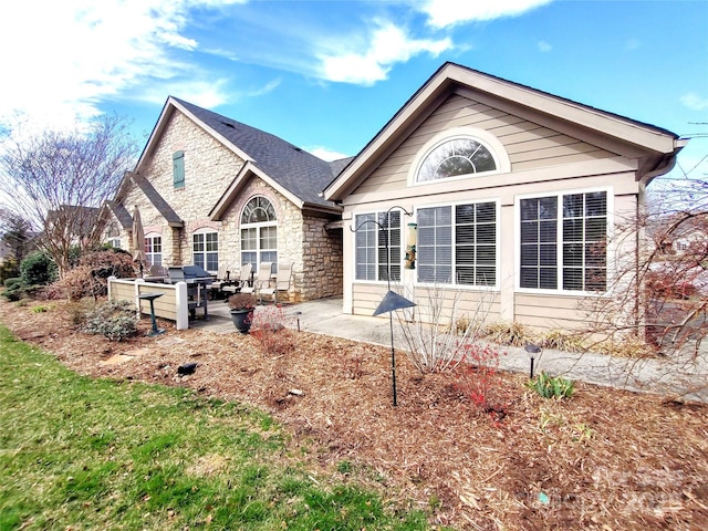 rear view of property with a patio area, stone siding, french doors, and roof with shingles