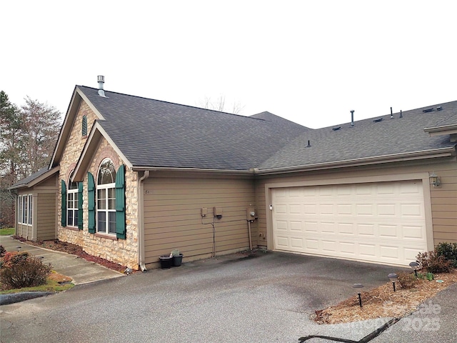 view of side of property featuring aphalt driveway, stone siding, a garage, and a shingled roof