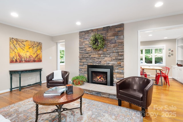 living room featuring light wood-style flooring, a fireplace, crown molding, and baseboards