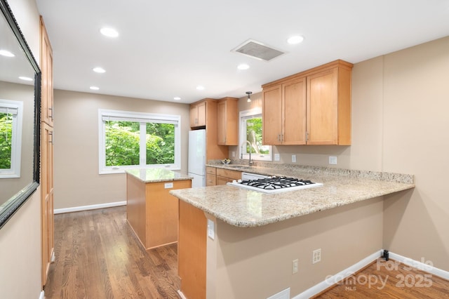 kitchen with a sink, a kitchen island, wood finished floors, white appliances, and a peninsula