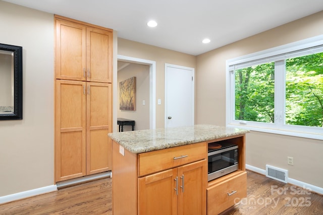 kitchen featuring stainless steel microwave, light stone countertops, visible vents, and light wood finished floors