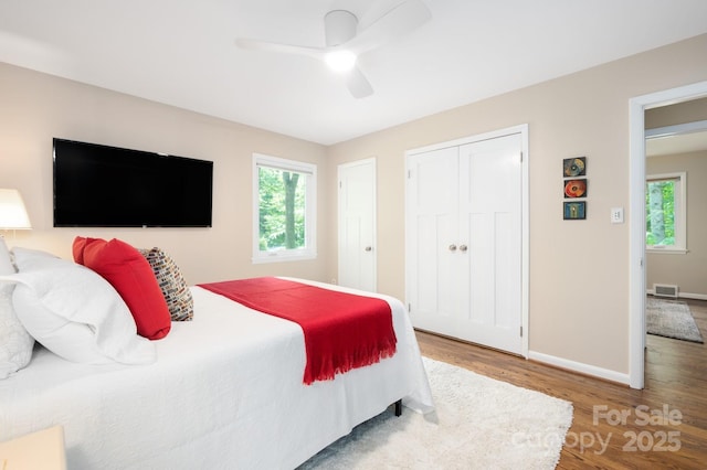 bedroom featuring wood finished floors, visible vents, baseboards, ceiling fan, and a closet