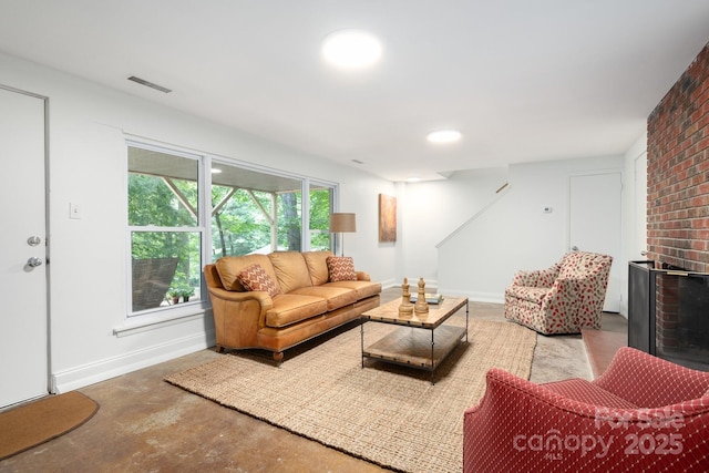 living room featuring visible vents, a brick fireplace, unfinished concrete floors, and baseboards