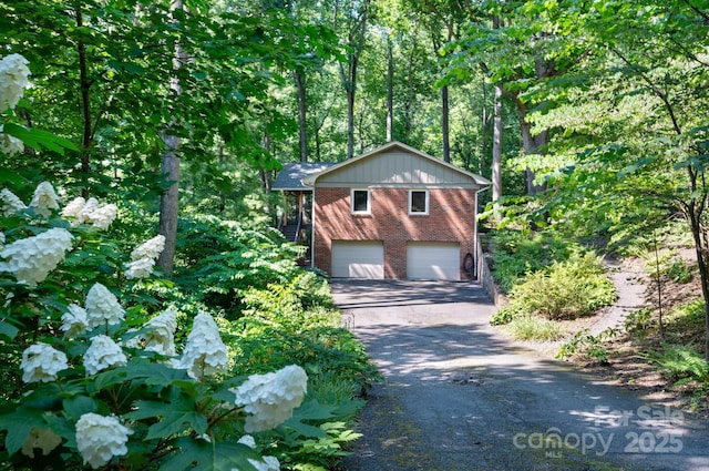 view of front of home with aphalt driveway, a view of trees, brick siding, and an attached garage