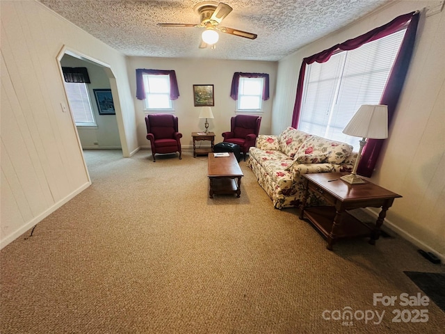 living room with arched walkways, ceiling fan, a textured ceiling, light colored carpet, and wood walls