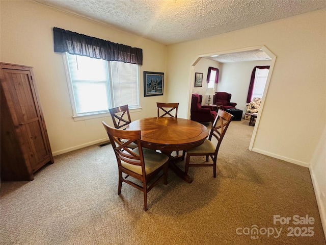 dining area featuring baseboards, carpet, arched walkways, and a textured ceiling