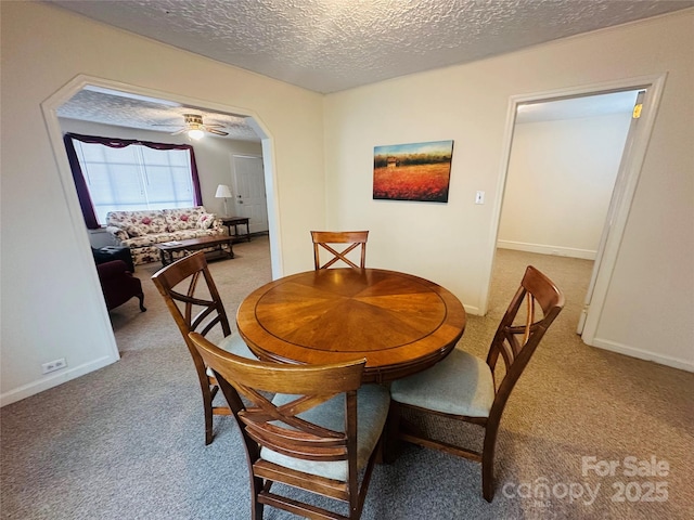 dining space with arched walkways, light carpet, a textured ceiling, and baseboards