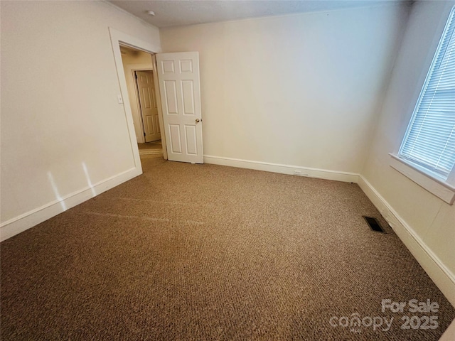 spare room with carpet floors, visible vents, and baseboards