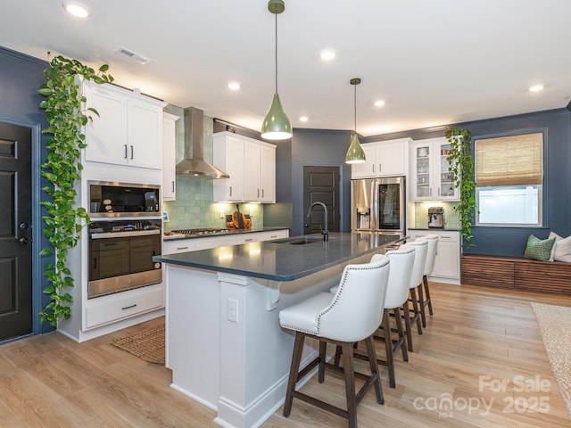 kitchen featuring a breakfast bar, dark countertops, stainless steel appliances, light wood-style floors, and wall chimney exhaust hood