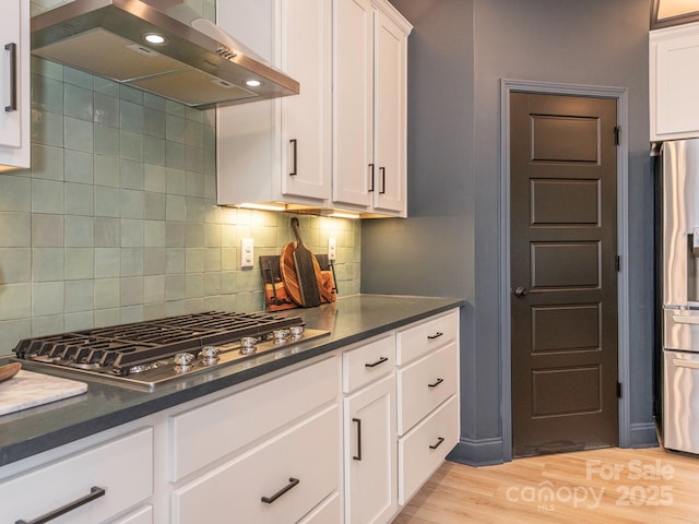 kitchen with light wood-type flooring, tasteful backsplash, range hood, white cabinetry, and stainless steel appliances