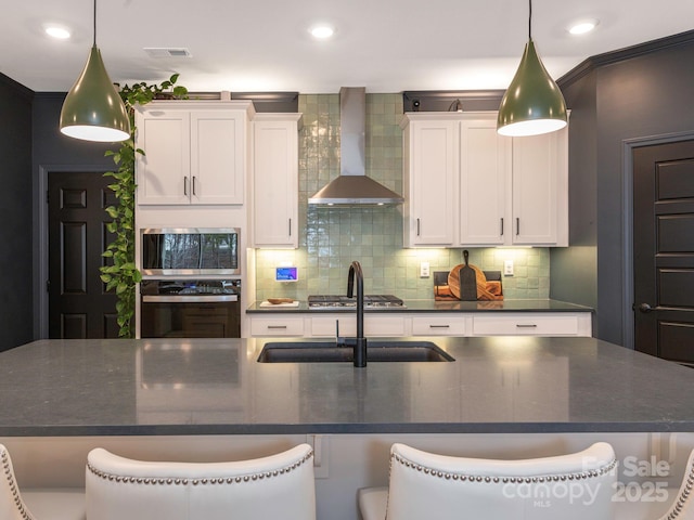 kitchen featuring white cabinetry, decorative backsplash, wall chimney exhaust hood, and visible vents