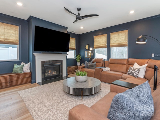 living area featuring ceiling fan, a fireplace with flush hearth, a healthy amount of sunlight, and wood finished floors