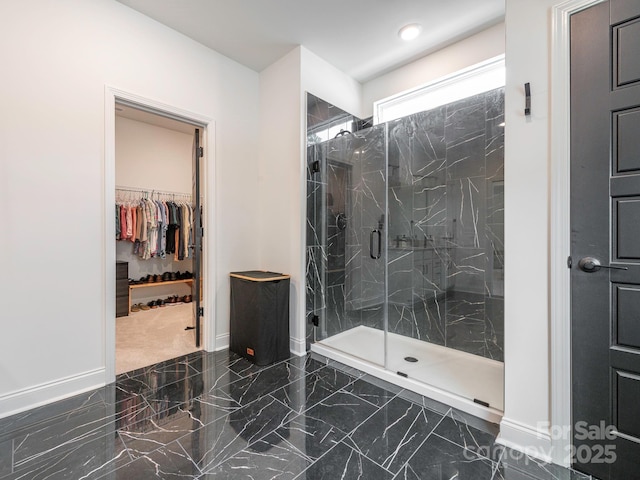 bathroom with a spacious closet, baseboards, marble finish floor, and a marble finish shower